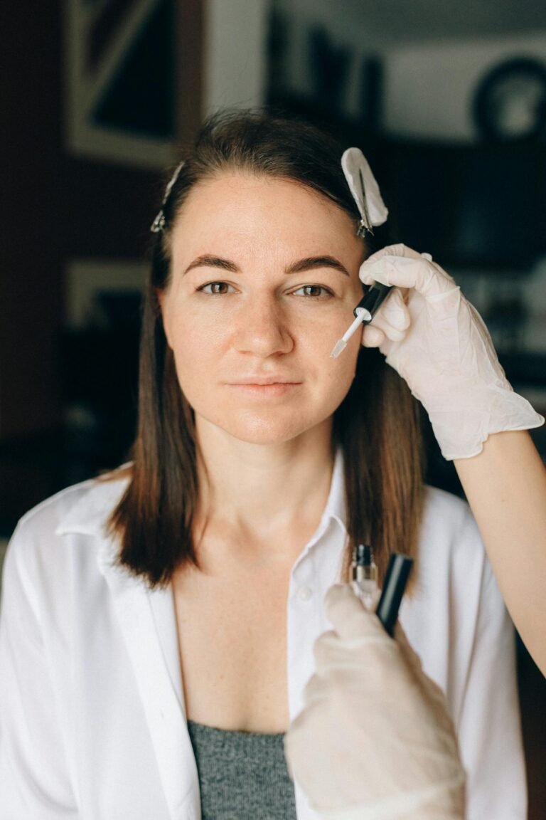 A cosmetologist applies skincare treatment to a woman indoors, focusing on facial care and beauty enhancement.