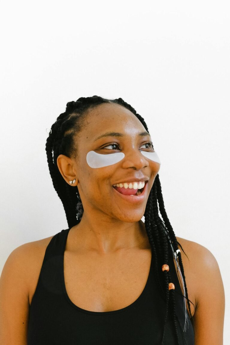 A smiling black woman with eye masks and braided hair captured in a bright portrait.