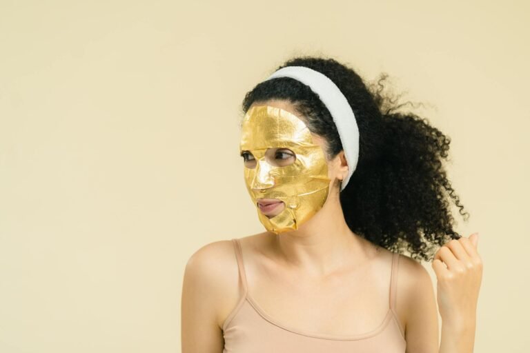 Stylish woman wearing a gold facial mask with a confident look against a yellow background.